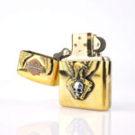 Orijinal Zippo Armor çakmak, gold gövdesi, Harley-Davidson teması, kartal ve kurukafa detaylı kabartmalı tasarımıyla öne çıkan kalın gövdeli premium Zippo çakmak modeli – Ateş Premium Armor Zippo koleksiyonu.